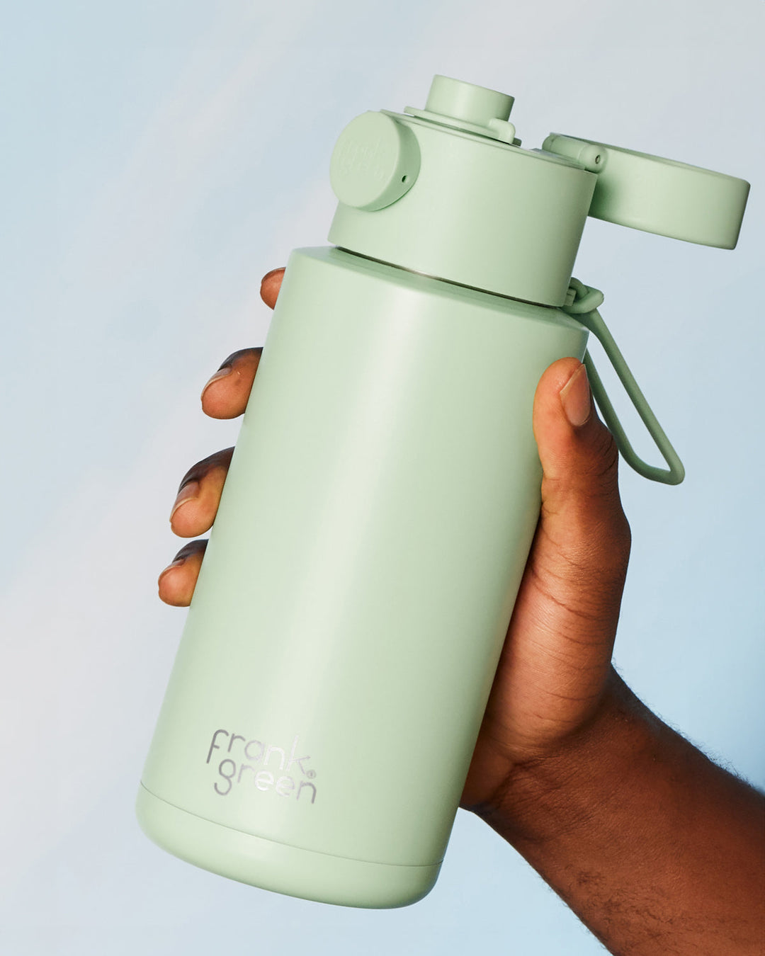 A hand holding a mint green Frank Green drink bottle with a switch lid.