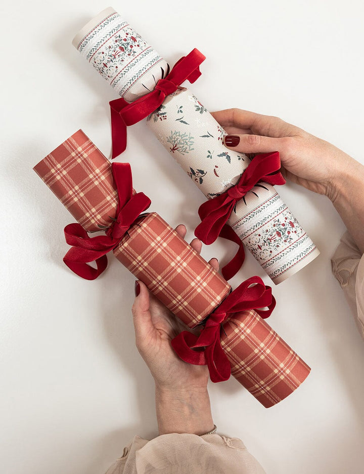 Two hands holding Christmas crackers with red ribbons on a white background