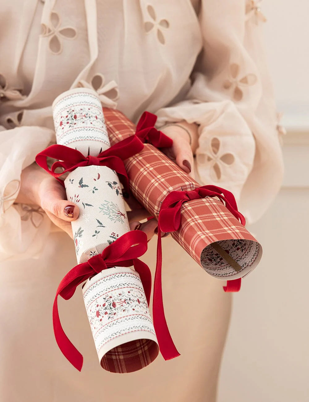 Christmas crackers with red ribbons held by a person wearing a light-colored outfit.
