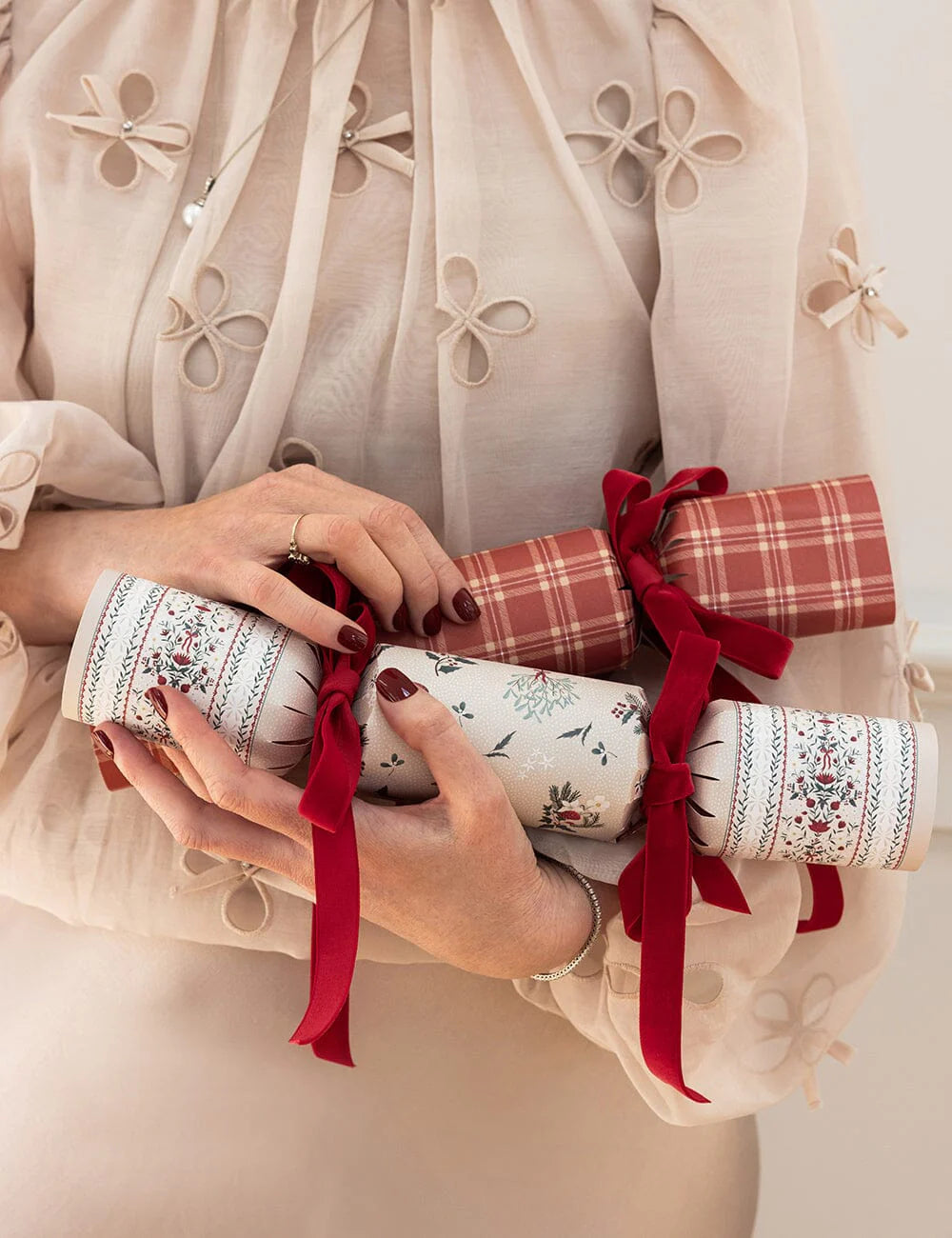 Hands holding a decorative cracker with intricate patterns and red ribbons against a light background.