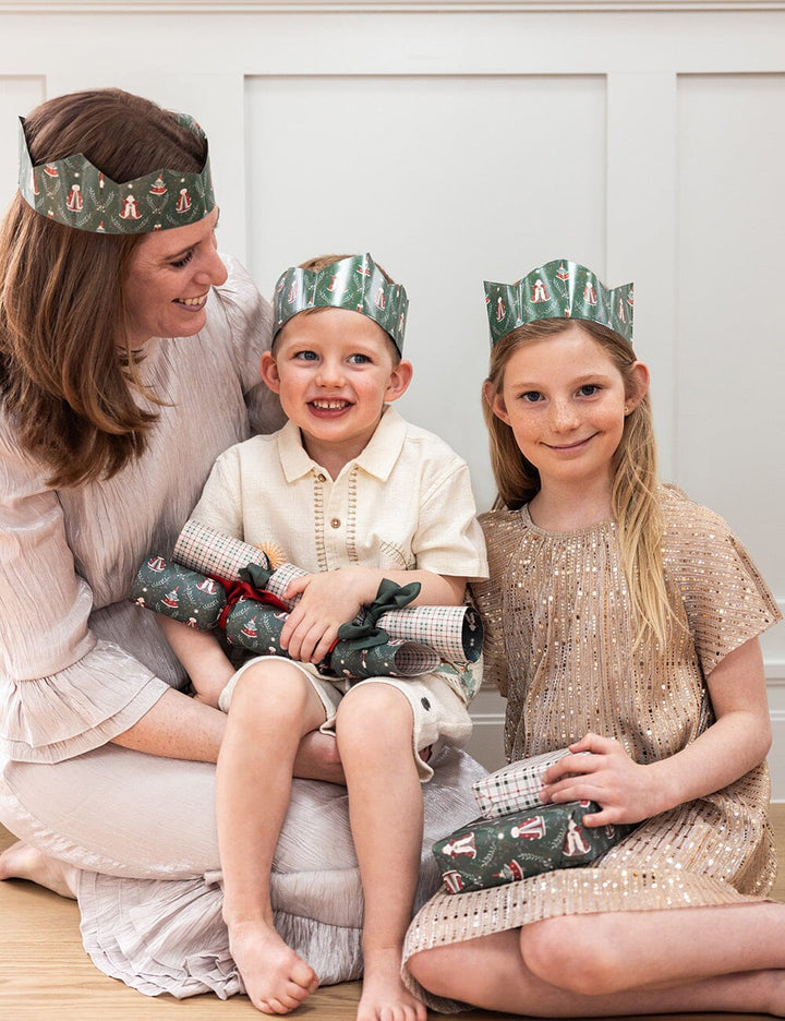 Woman and two children wearing festive crowns sitting on a white surface.