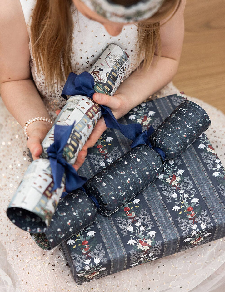 Person holding a wrapped gift with decorative paper and blue ribbon on a light surface.