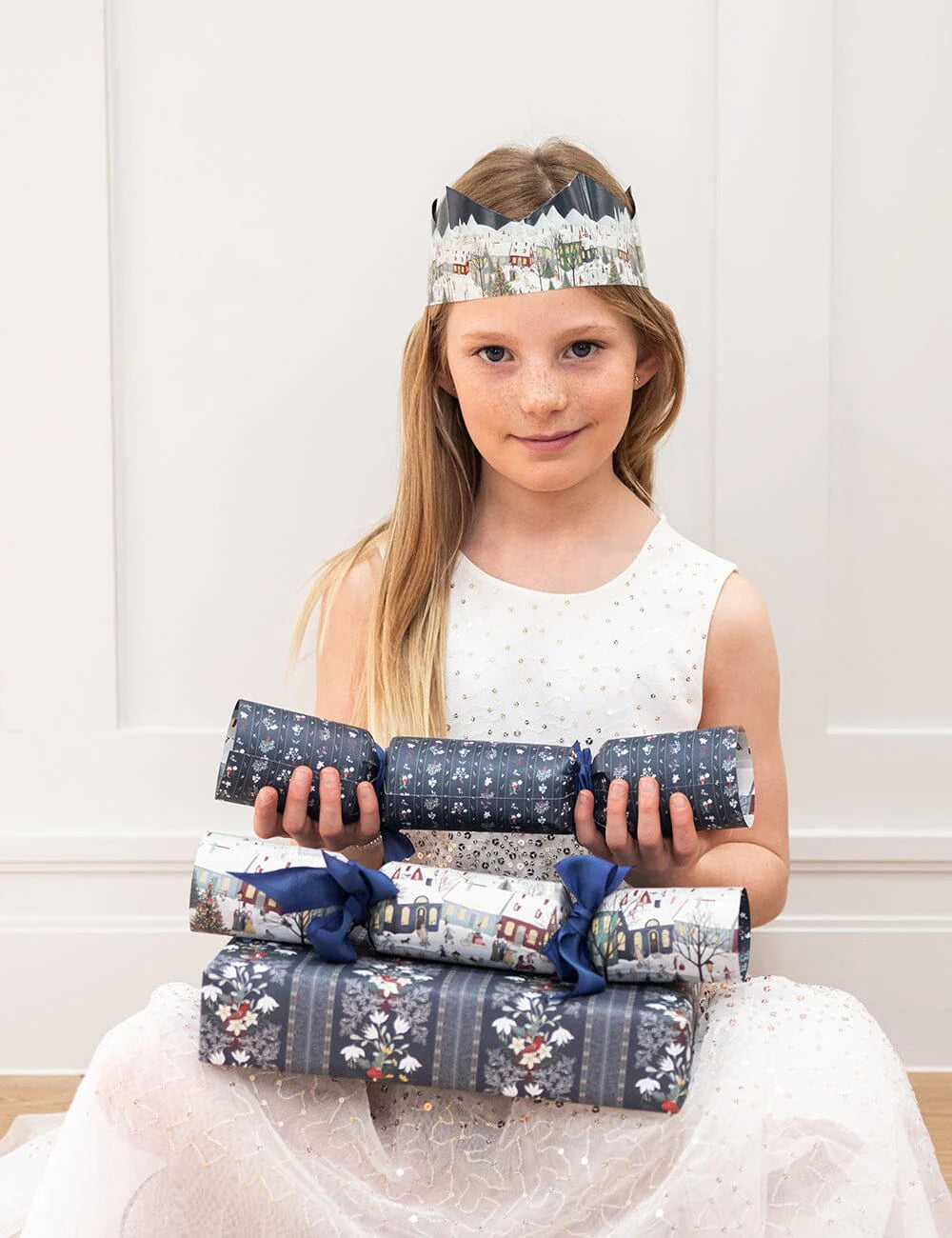 Young girl holding wrapped presents with a decorative headband against a white background