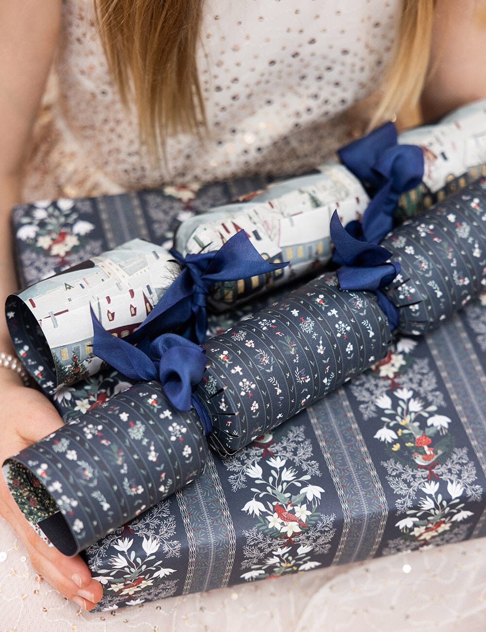 Decorative Christmas crackers with blue ribbons held by a person.