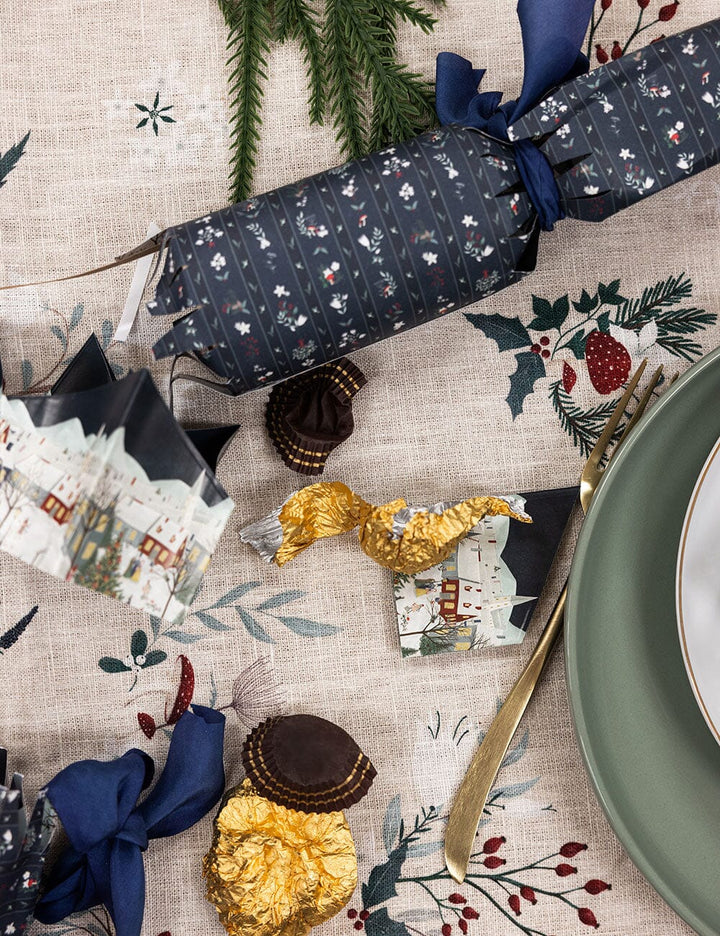 Decorative Christmas cracker on a festive table setting with crackers, gold paper, and holly leaves.