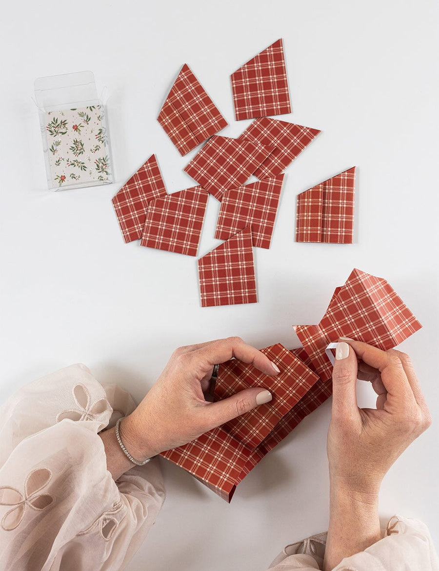Hands assembling red plaid paper crowns on a white background