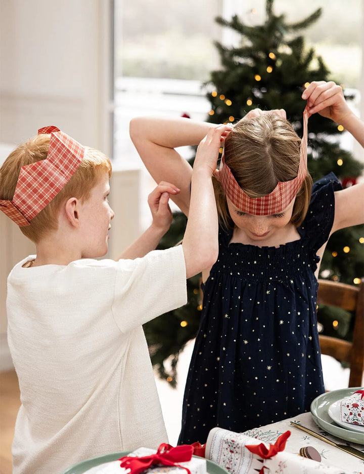 Two children wearing red checkered headbands in a festive setting with a Christmas tree.