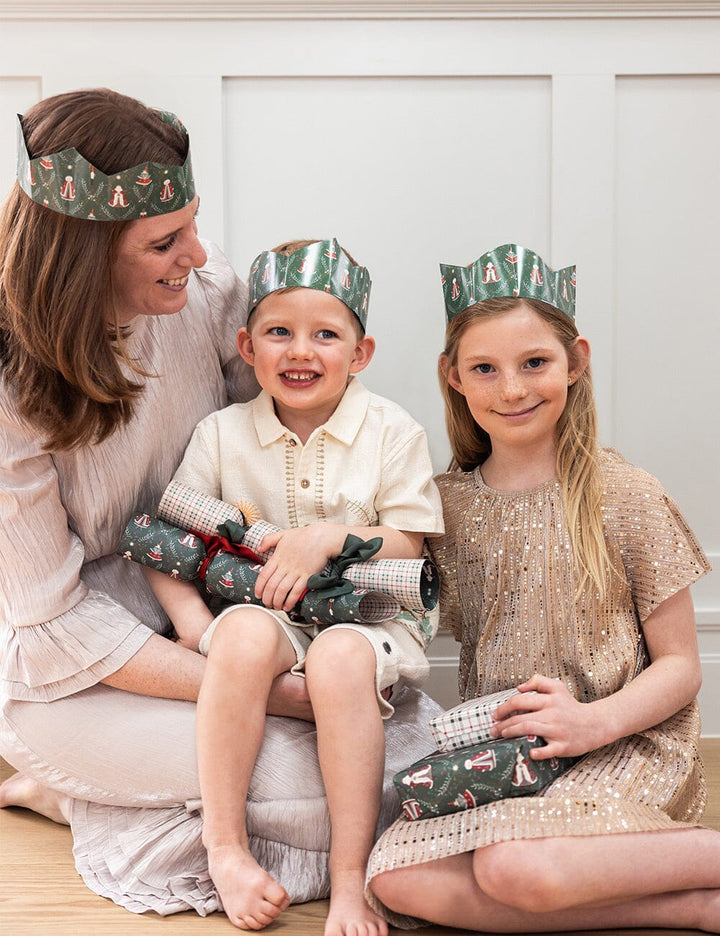 Woman and two children wearing festive crowns, sitting on a white surface.