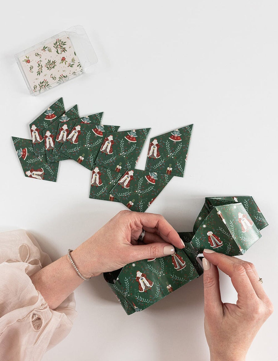 Hands arranging green patterned paper crowns on a white surface