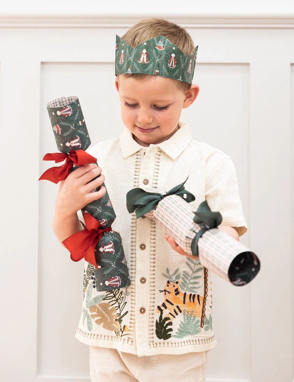Child wearing a festive paper crown and holding Christmas crackers against a white background