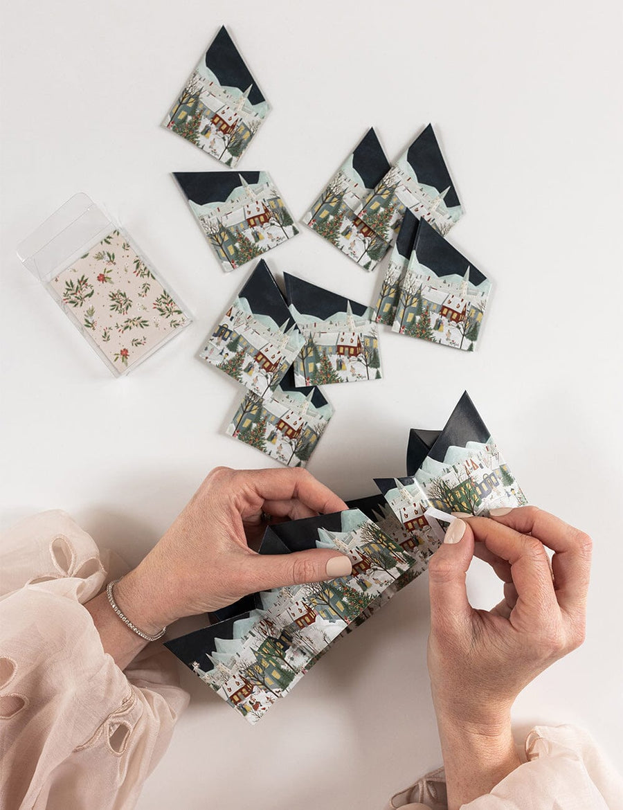 Hands arranging paper crowns with scenic designs on a light surface