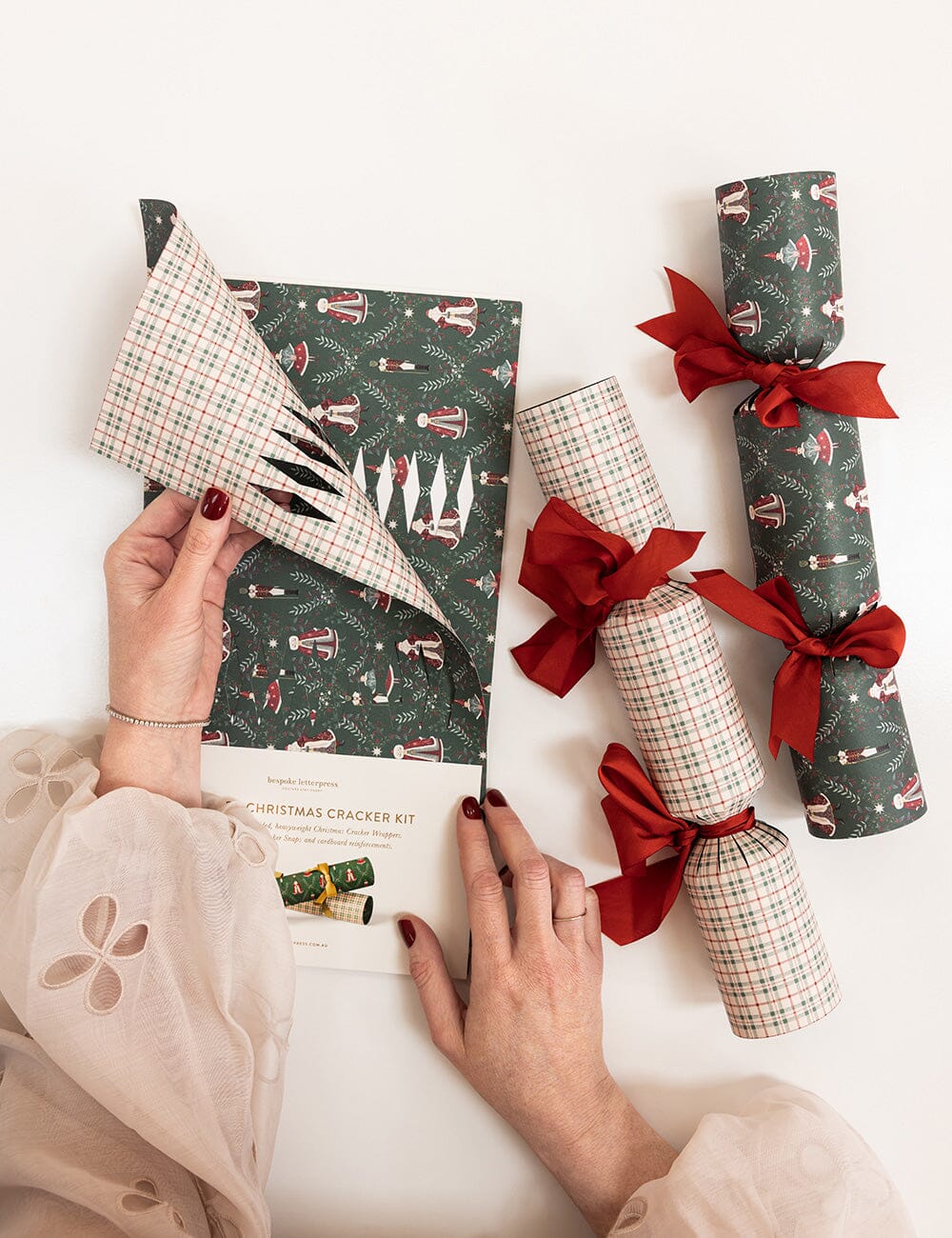 Person assembling a Christmas cracker kit with patterned paper and ribbons.