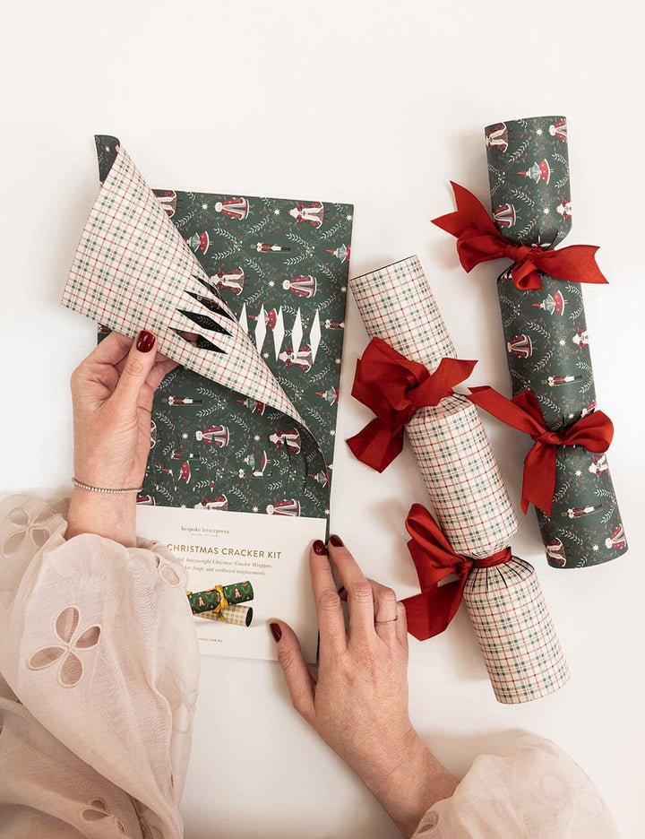 Person assembling a Christmas cracker kit with patterned paper and ribbons.