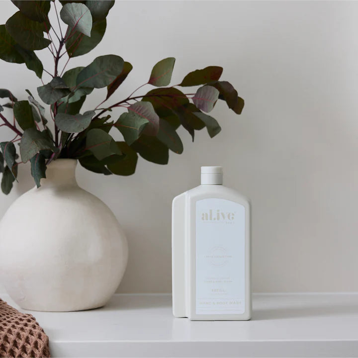 White bottle labeled 'alive' next to a white vase with greenery on a neutral background