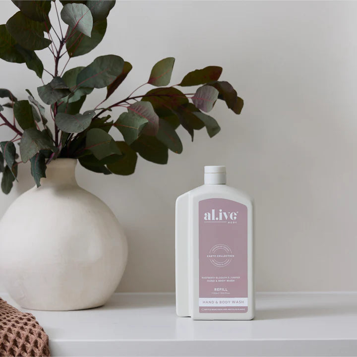 White bottle of 'alive' hand and body wash on a shelf with a vase and eucalyptus leaves in the background.