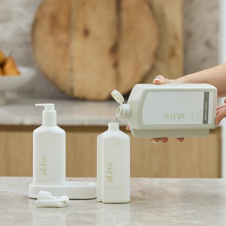 Person pouring liquid from a large bottle into smaller bottles on a countertop.