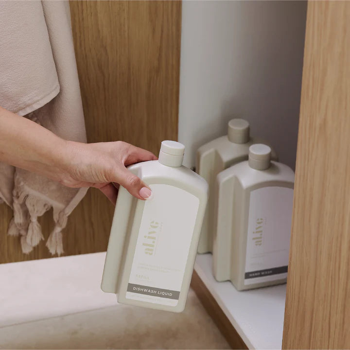 Person holding a bottle of 'alive' skincare product with more bottles in the background.