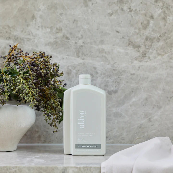 White bottle of dishwash liquid on a marble surface with a vase and flowers in the background.