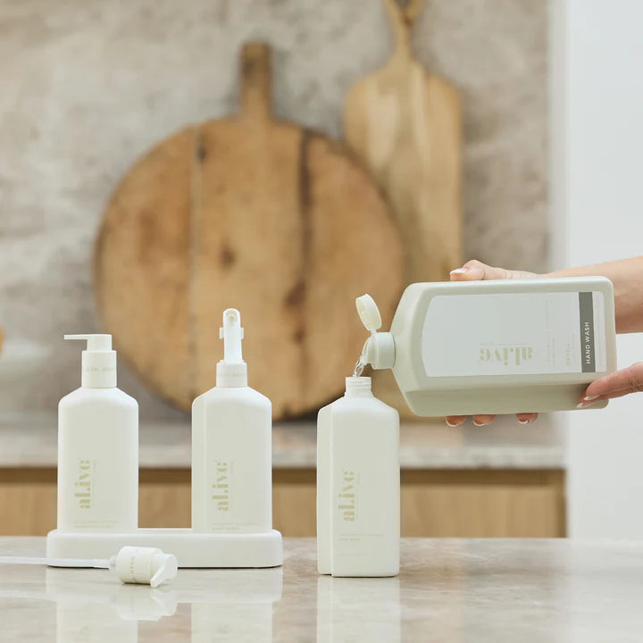 White bottles with 'alive' branding on a kitchen counter, with a person pouring liquid into one of the bottles.