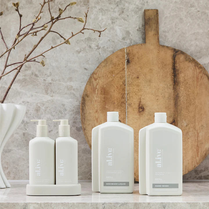 Set of white bottles with pump dispensers on a stone surface, with a wooden cutting board and branch in the background.