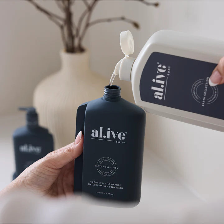 Person pouring body wash from a white bottle into a black 'al.ive' bottle on a neutral background.