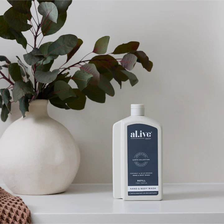 Hand and body wash refill bottle with 'alive' branding next to a vase with greenery on a white surface.