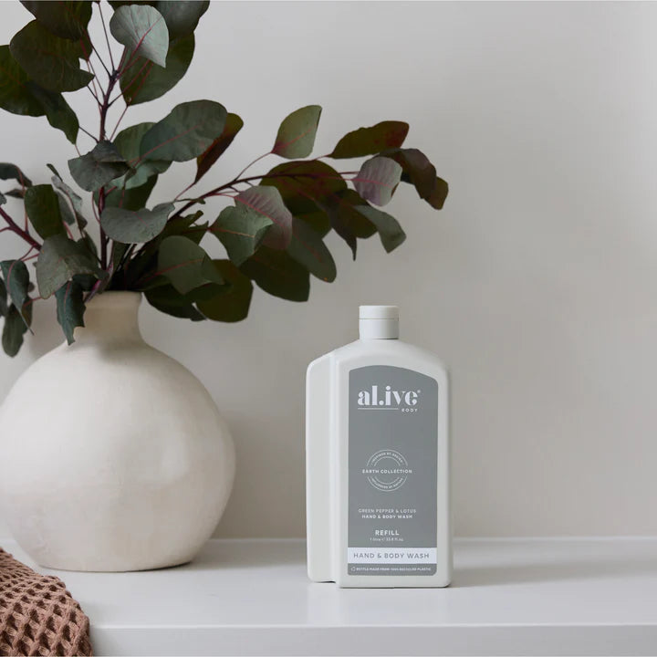 White bottle of 'alive' hand and body wash on a shelf with a vase and plant in the background.