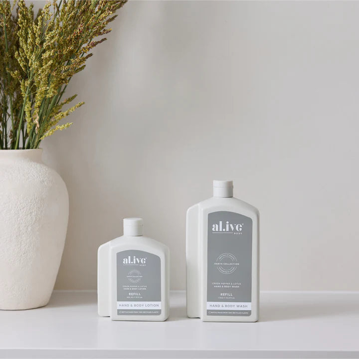 Two bottles of 'alive' products on a white surface with a vase of dried flowers in the background.