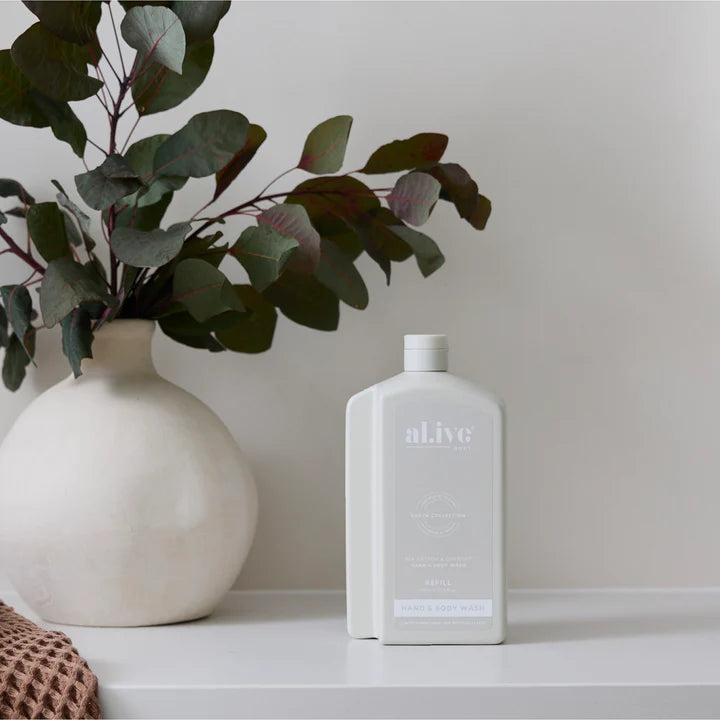 White bottle labeled 'aLlve' next to a vase with green leaves on a white surface.