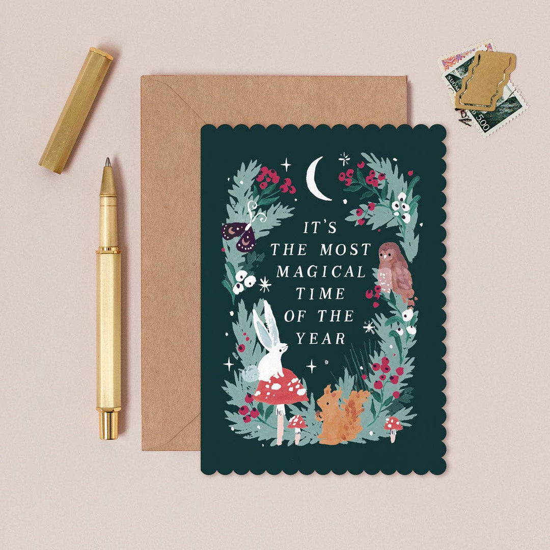 Greeting Christmas card with floral design and text, envelope, and pen on a beige background