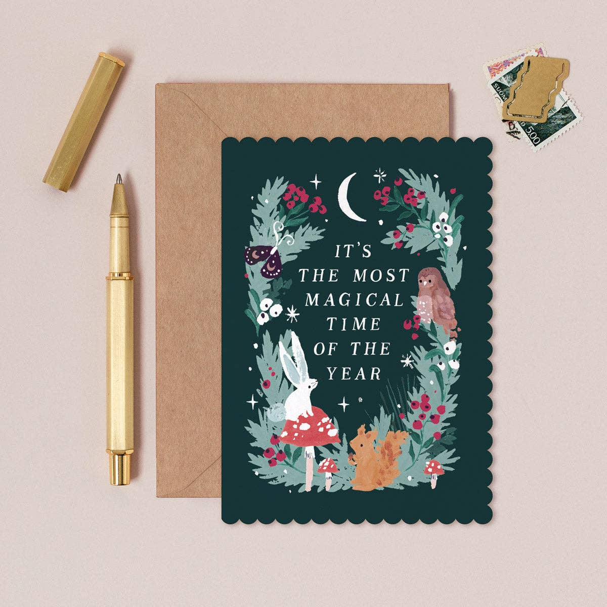 Greeting Christmas card with floral design and text, envelope, and pen on a beige background