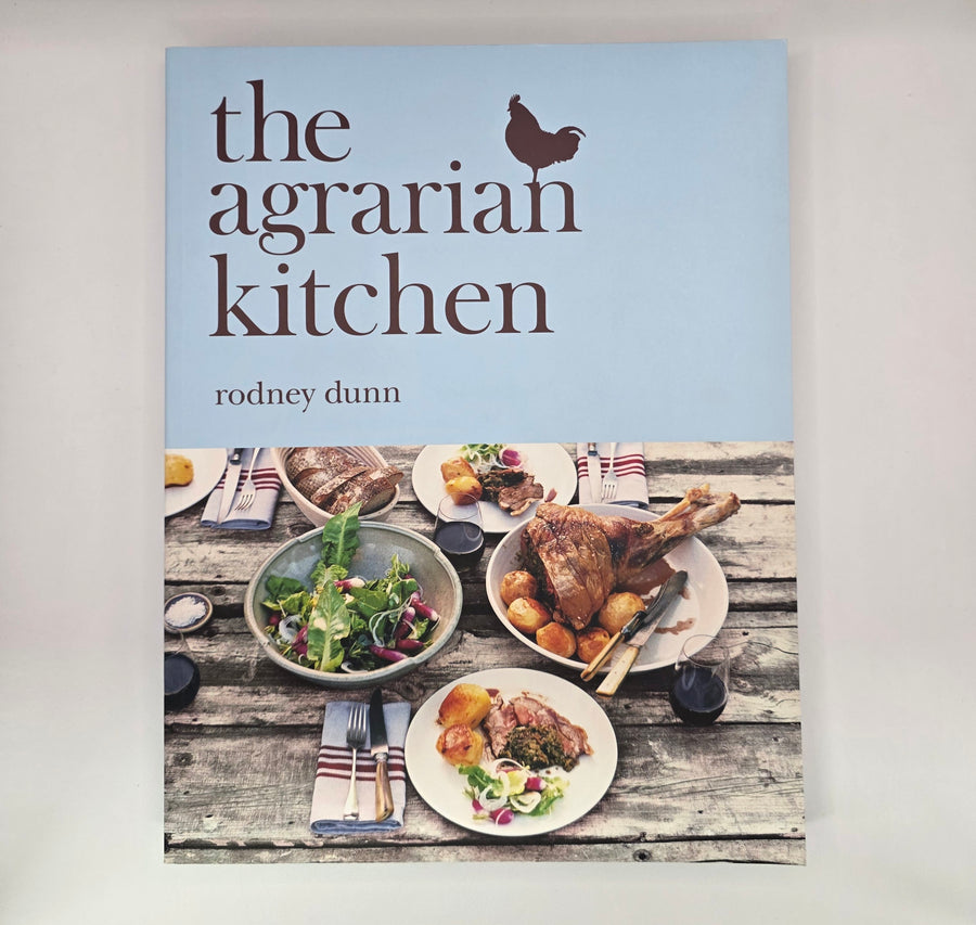 Book cover of 'The Agrarian Kitchen' by Rodney Dunn with images of food on a wooden table.