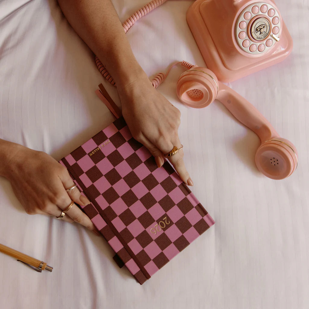 Person holding a pink and brown checkered clutch with a vintage pink phone in the background.