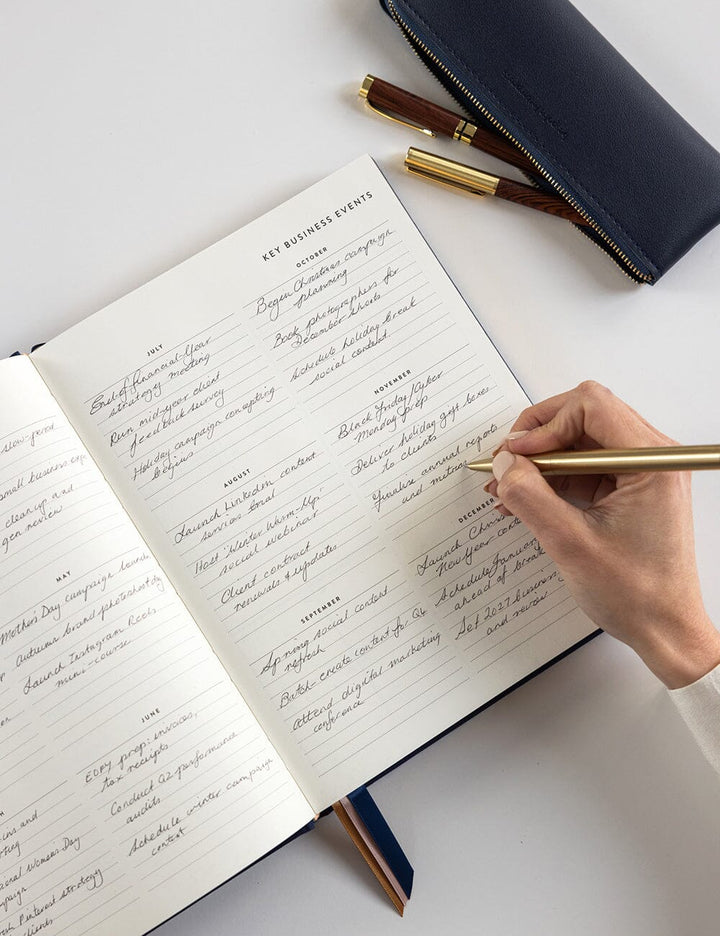 Hand writing in a notebook with a gold pen on a white surface