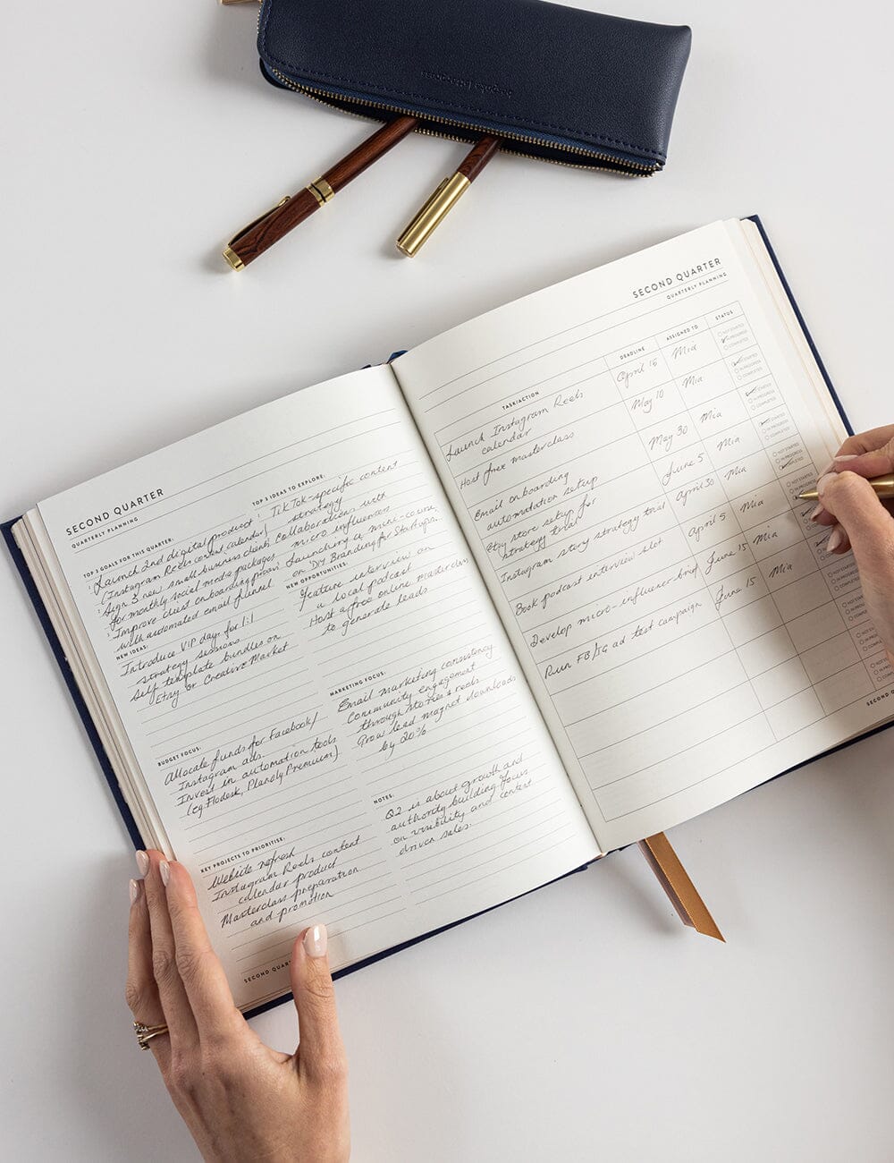 Person writing in an open notebook with a pen on a white surface