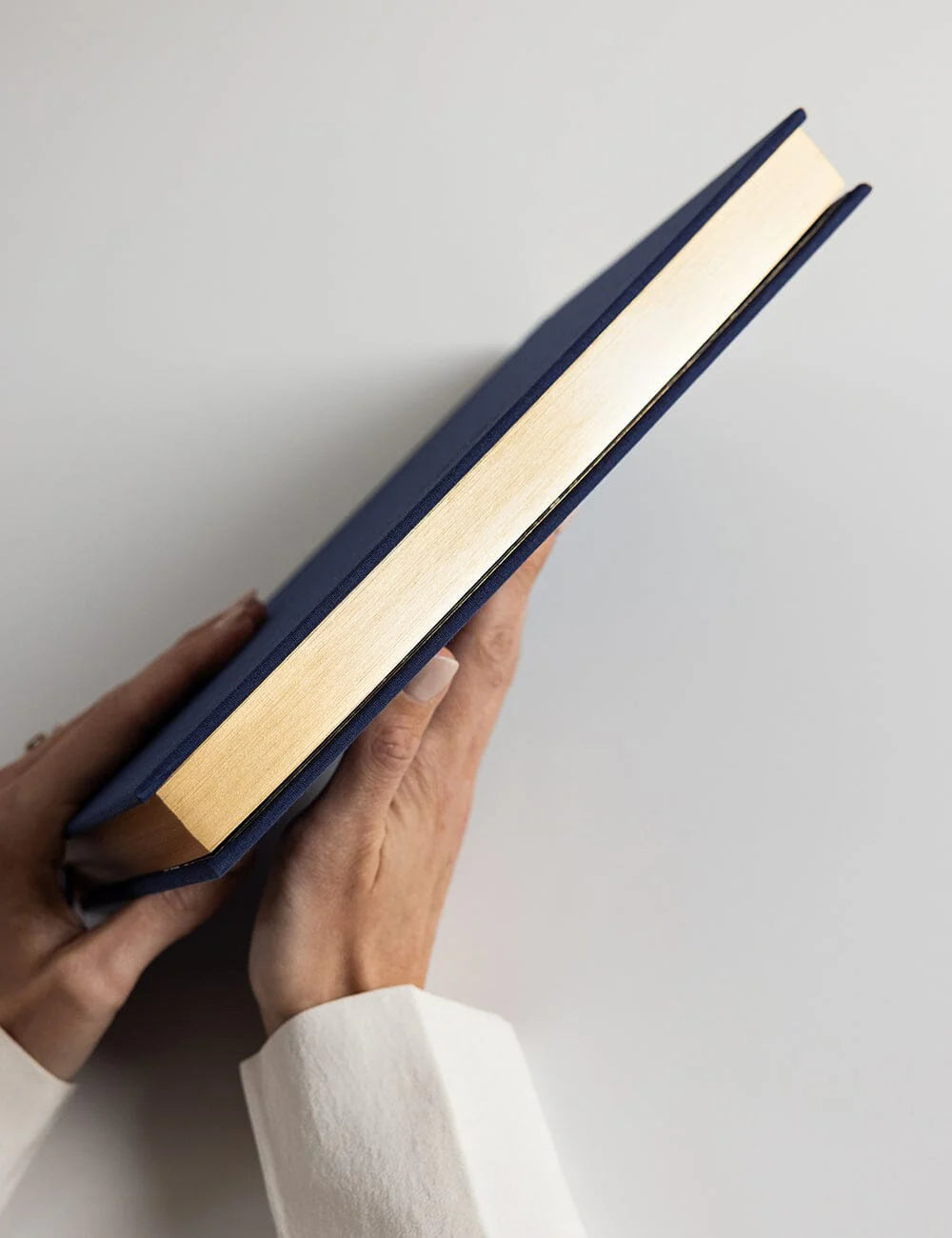 Hand holding a blue book with gold edges against a light gray background