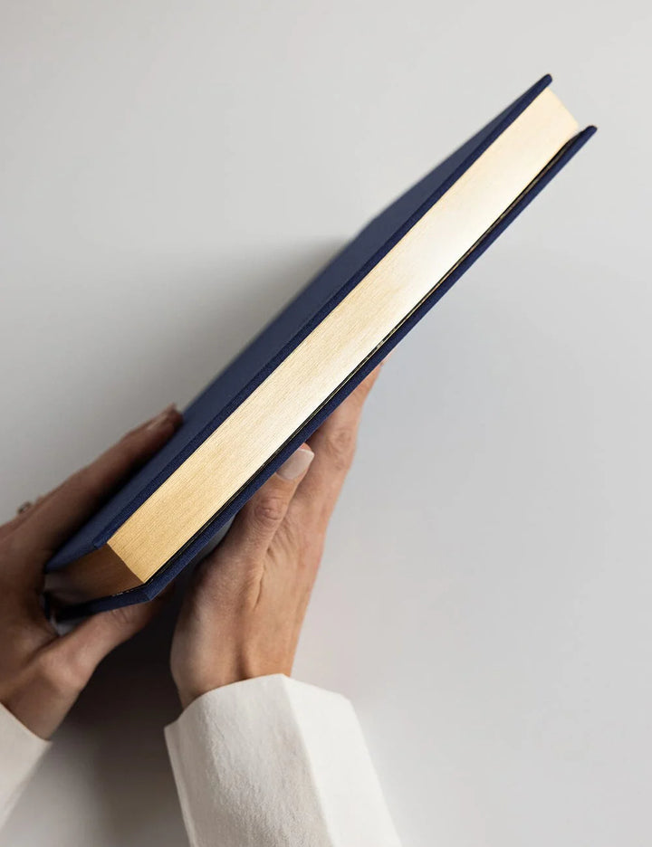 Hand holding a blue book with gold edges against a light gray background