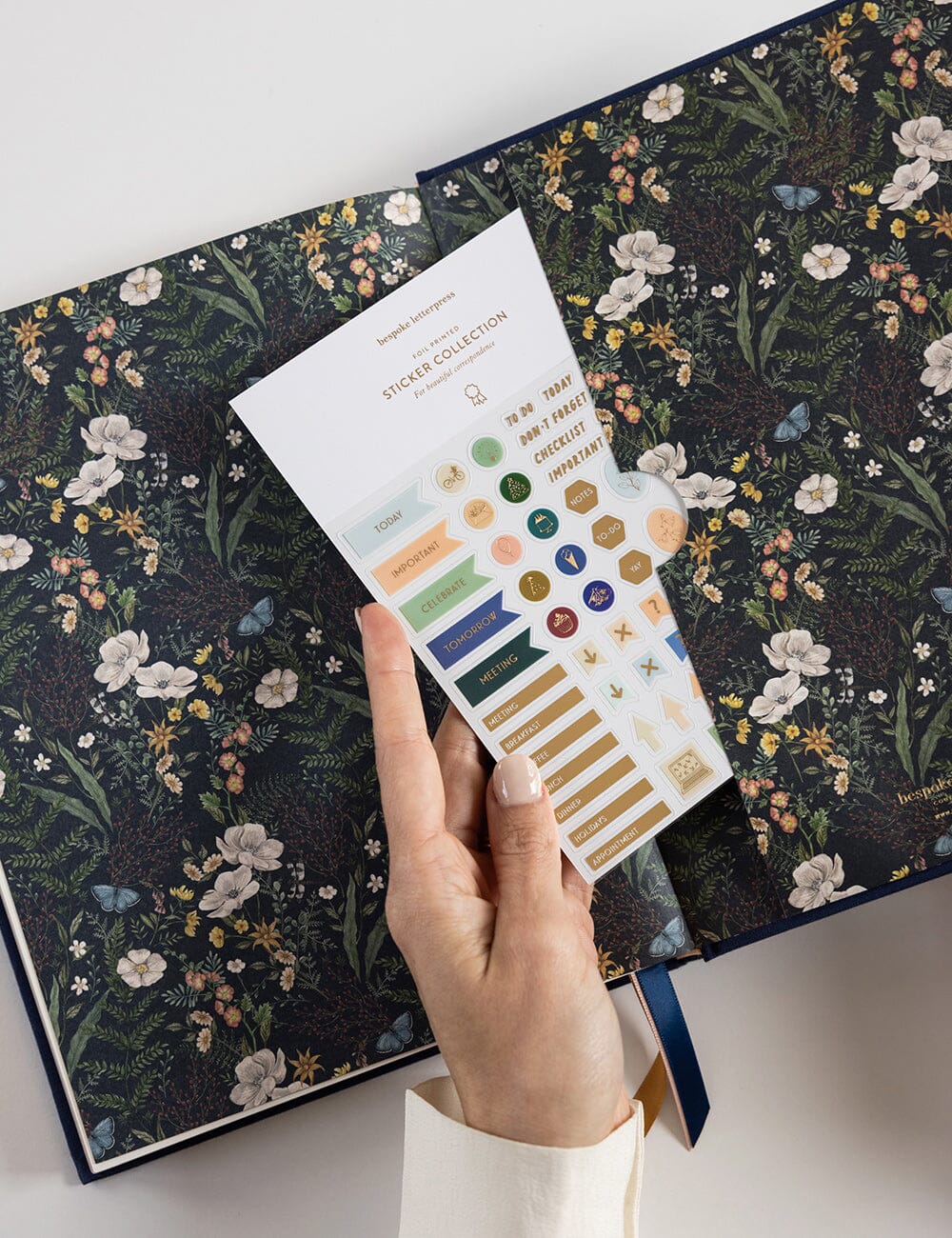 Hand holding a sticker sheet with decorative elements over a floral-patterned book