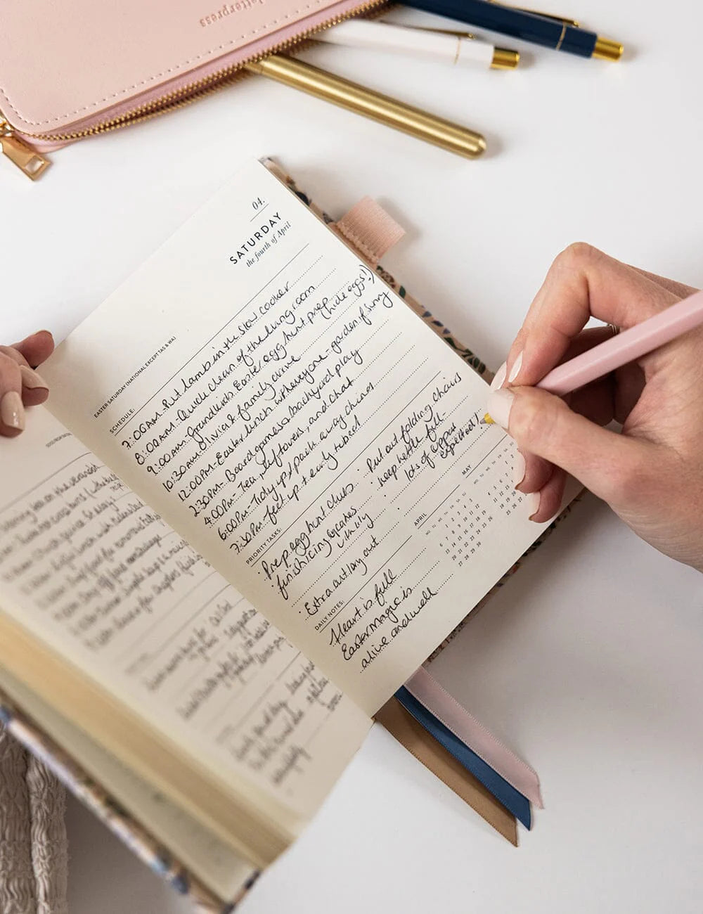 Person writing in a planner with a pink pen on a white surface