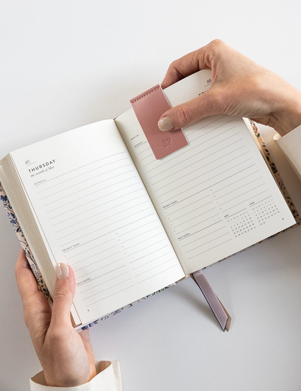 Person holding an open planner with a pink leather cover on a light gray background