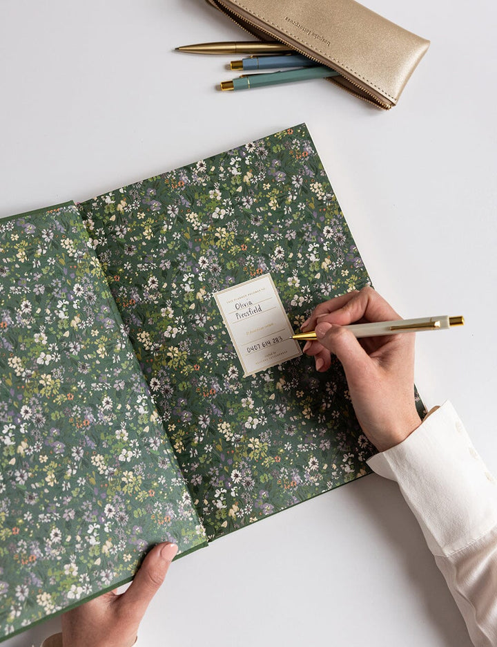 Floral notebook with a hand holding a pen on a white surface