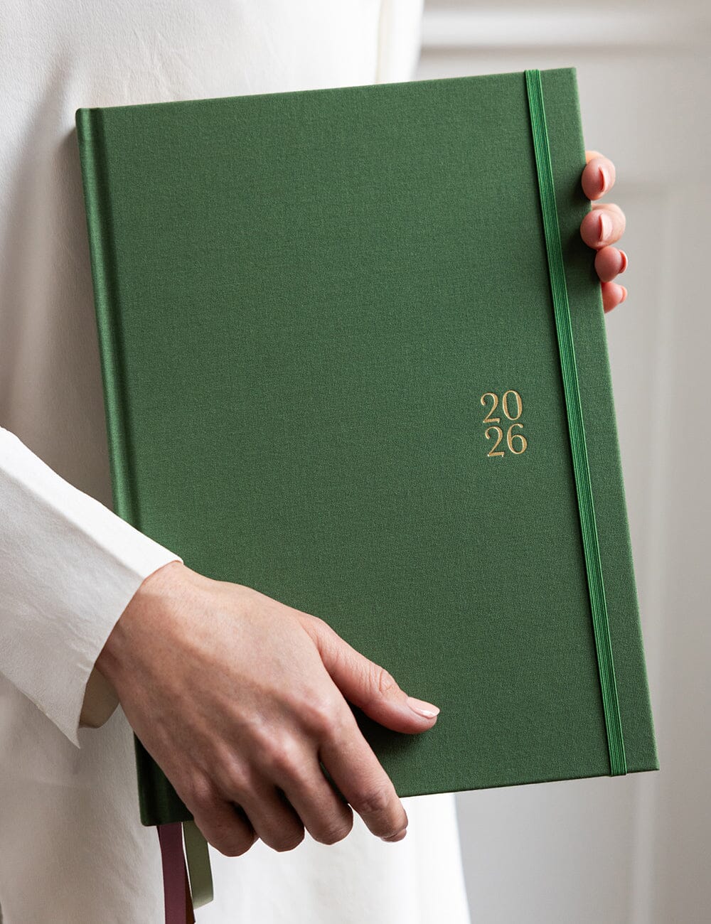 Green calendar with '2026' on the cover held by a person wearing a white shirt.