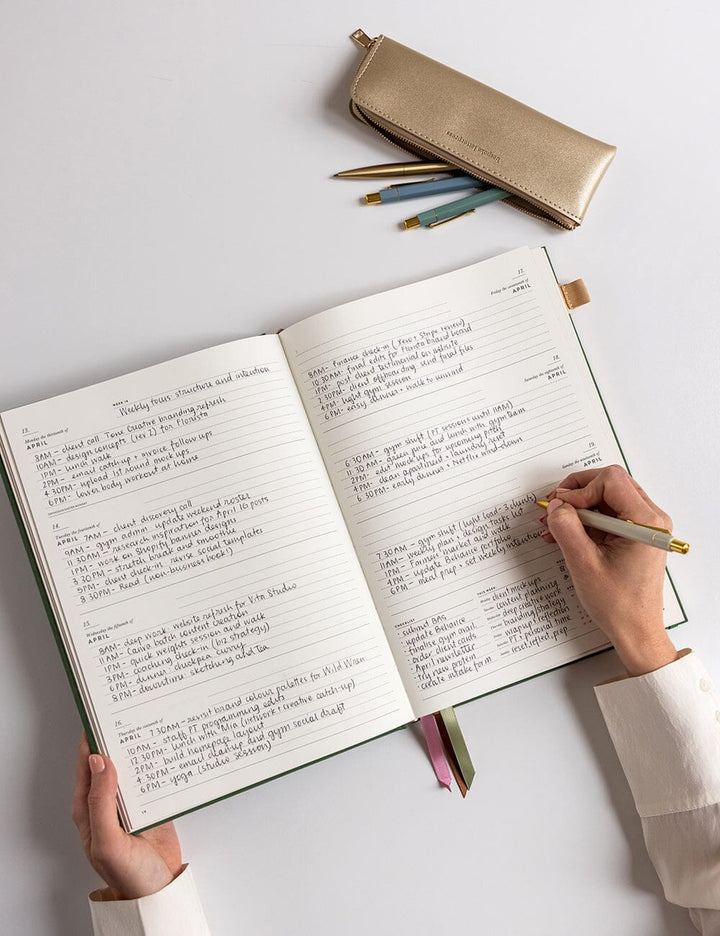 Person writing in an open notebook with a pencil on a light surface
