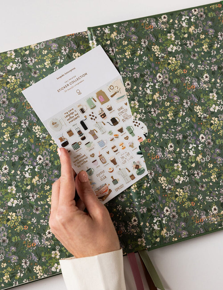 Hand holding a sheet of stickers over a floral-patterned book