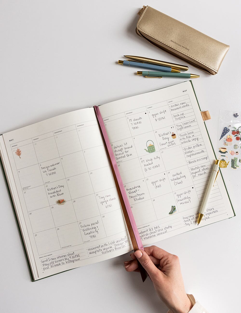 Open planner with notes and a gold pencil case on a white surface