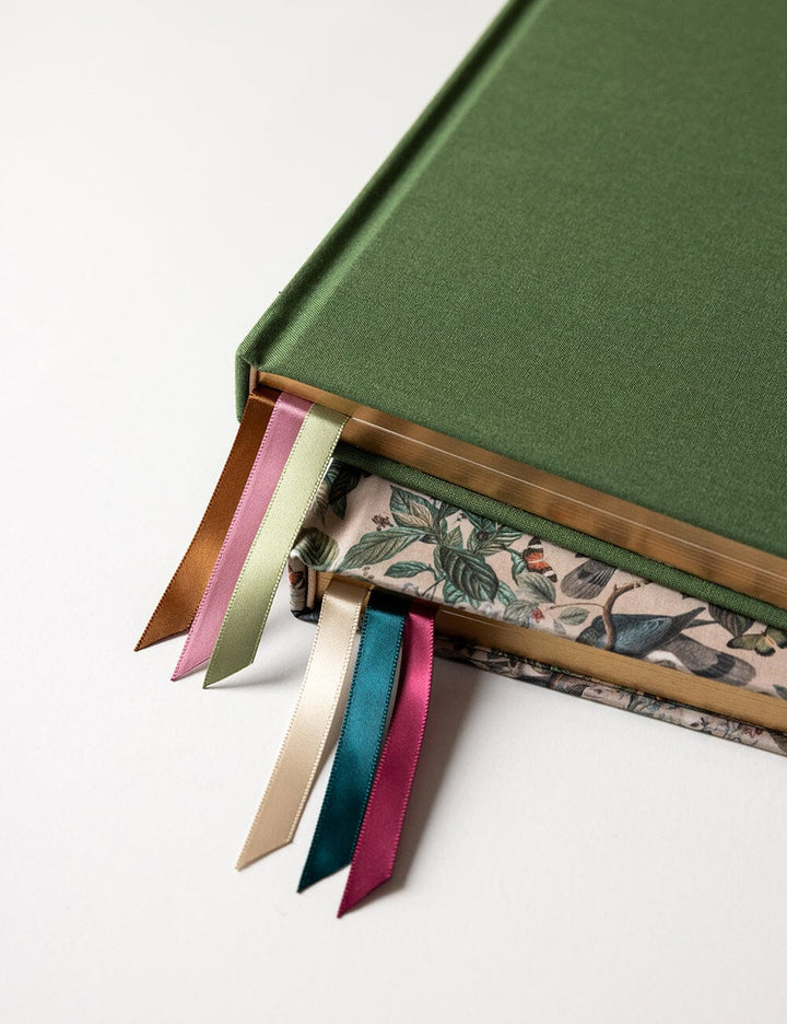 Green notebook with floral design on the cover and colorful ribbon markers on a white background