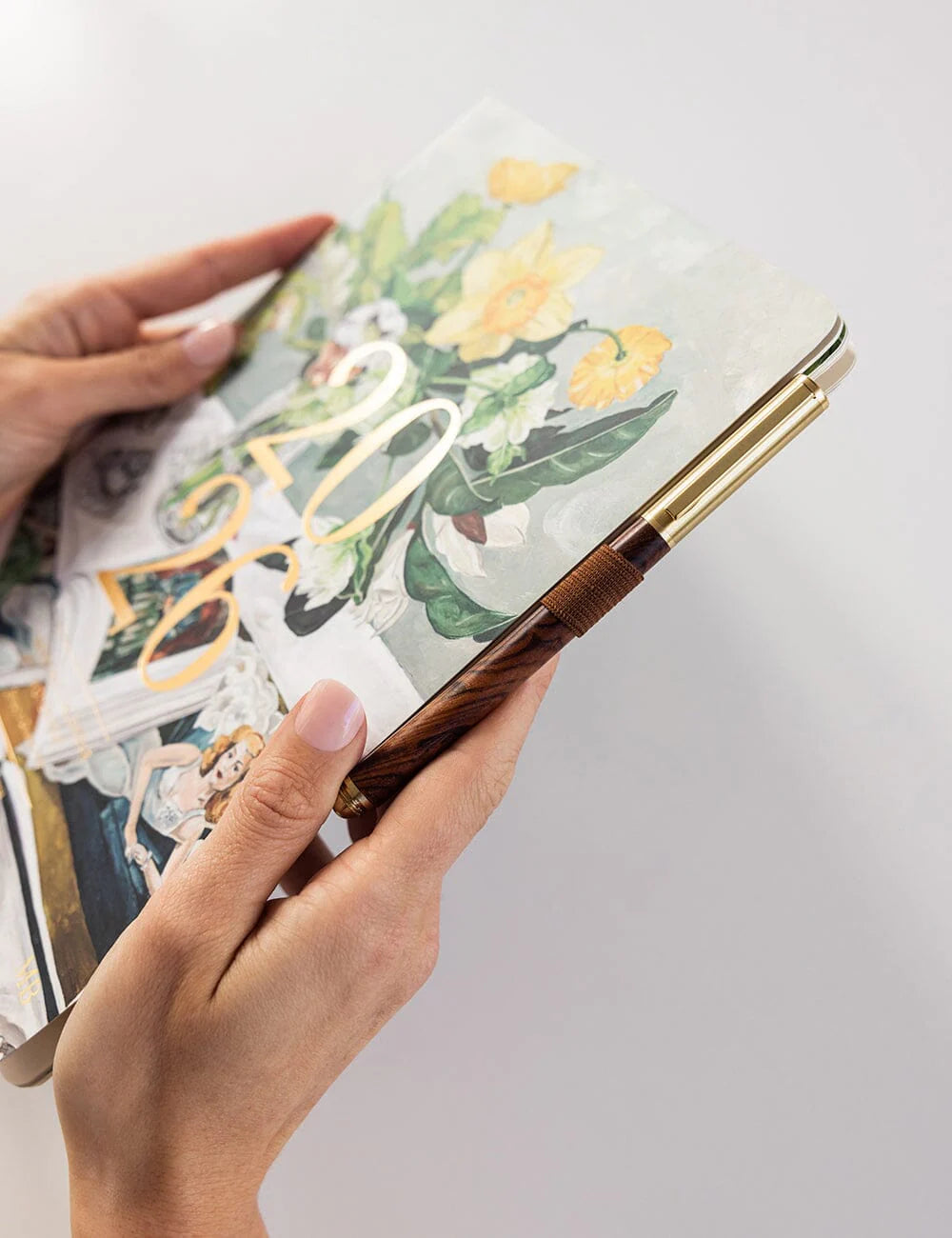 Hand holding a decorative pen over a notebook with floral design