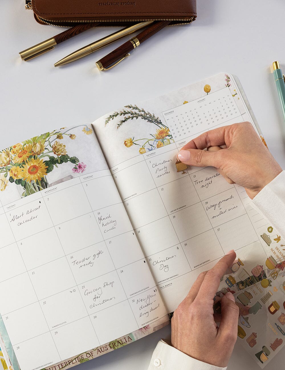 Person using a planner with floral designs and a hand holding a small object.