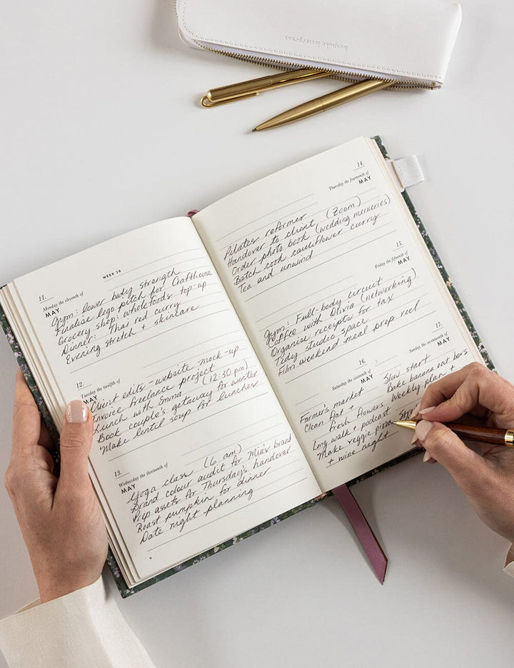 Person writing in a notebook with a pen on a white surface