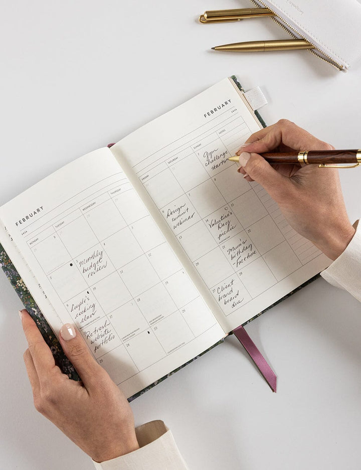 Person writing in a planner with a pen on a white surface